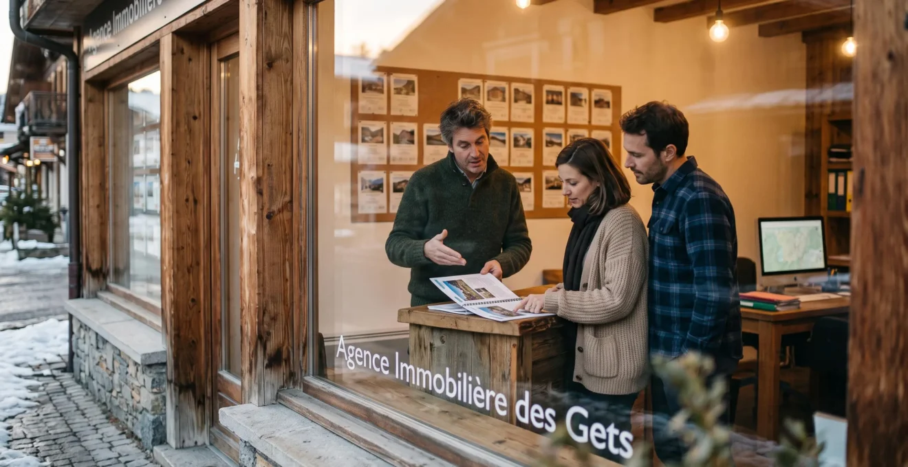 Un agent immobilier présente un dossier de vente à un couple d'acquéreurs dans une agence de village de montagne.